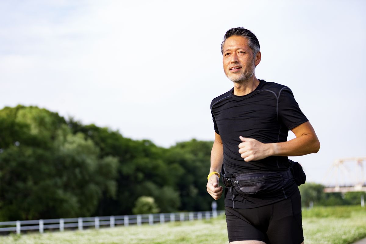 active japanese senior man jogging against the sunshine